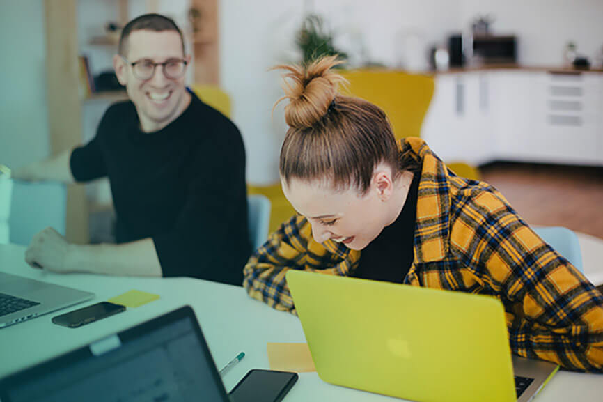 Woman in a yellow tartan blazer laughs with a coworker during a meeting